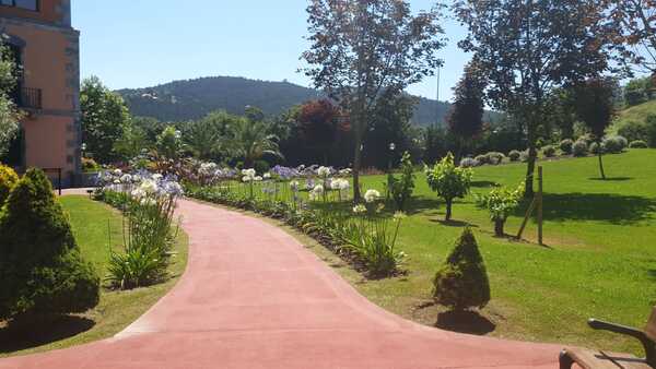 Sendero rojizo que atraviesa un jardín con Agapanthus (lirios africanos) blancos y azules, rodeado de césped y árboles