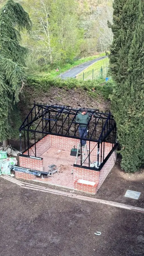 Vista aérea de un operario trabajando en el interior de la estructura metálica de aluminio negro de un invernadero victoriano sin acristalar.