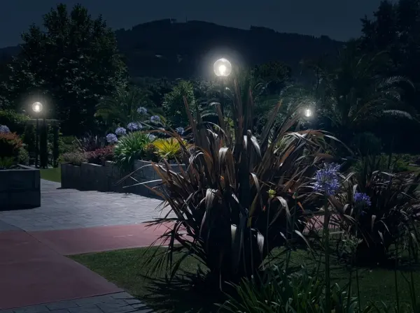 Jardín iluminado de noche con farolas de globo, seto topiario y macizo floral con agapantos blancos en Lekeitio